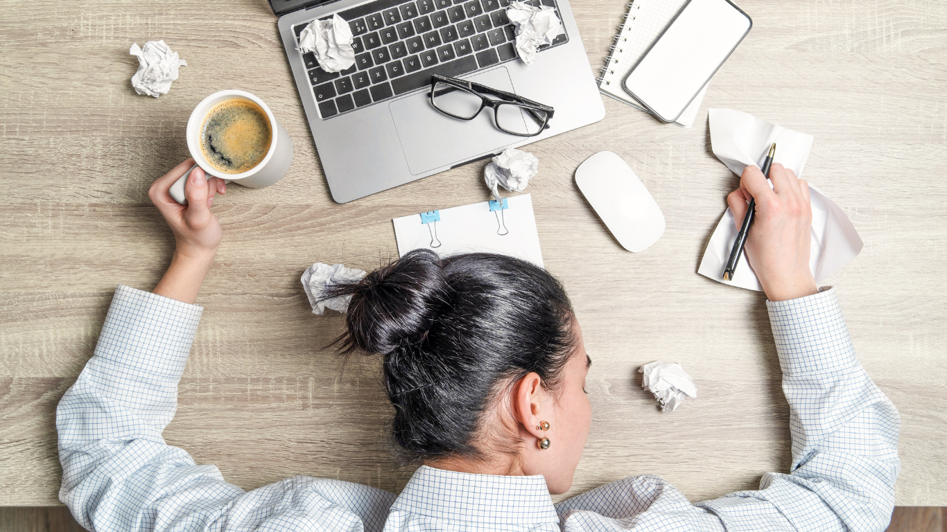 an over-tired worker sleeping at a messy desk in front of a laptop